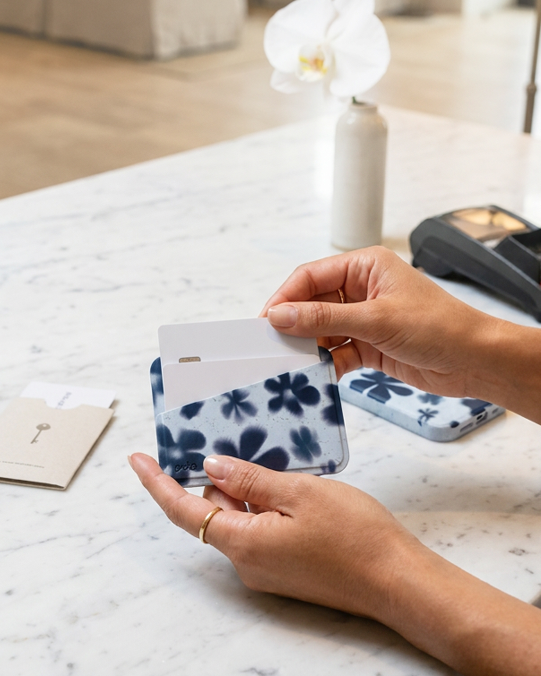 A person's hands hold a blue floral card wallet, removing a card over a marble countertop.