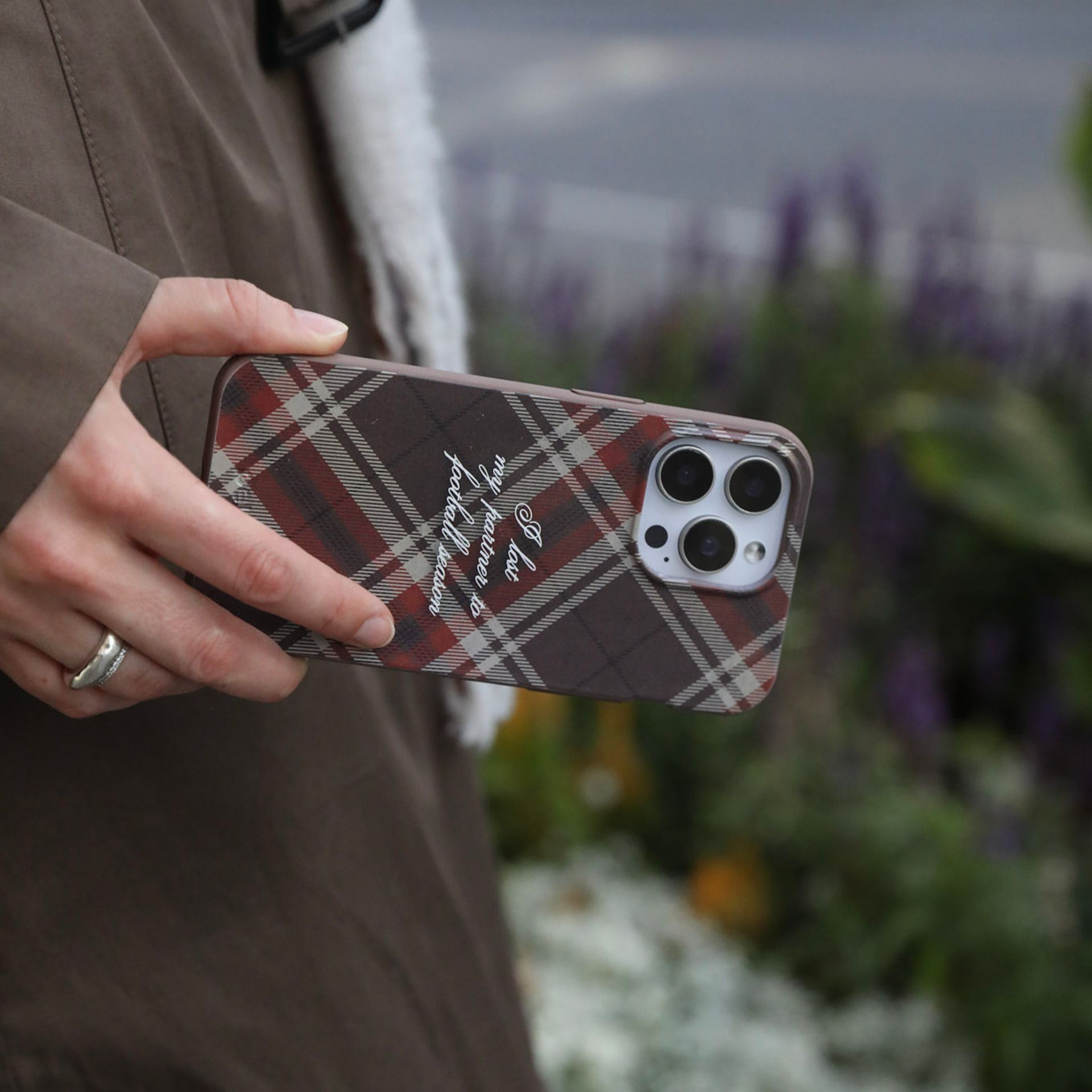 A person holds a phone with a brown and red plaid case that reads, 'I lost my partner to football season'.