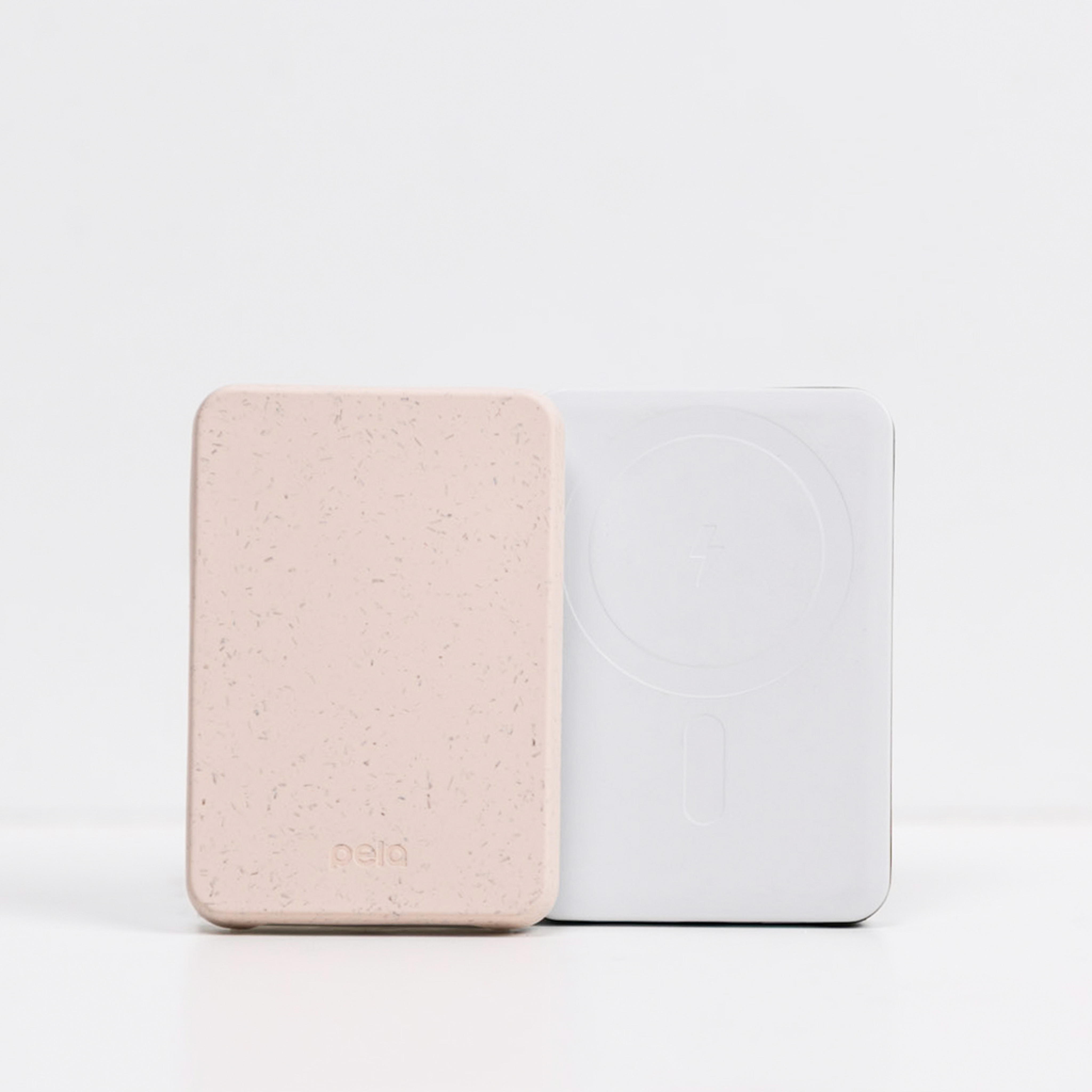A pink, speckled Pela portable charger stands next to a white portable charger against a white background.
