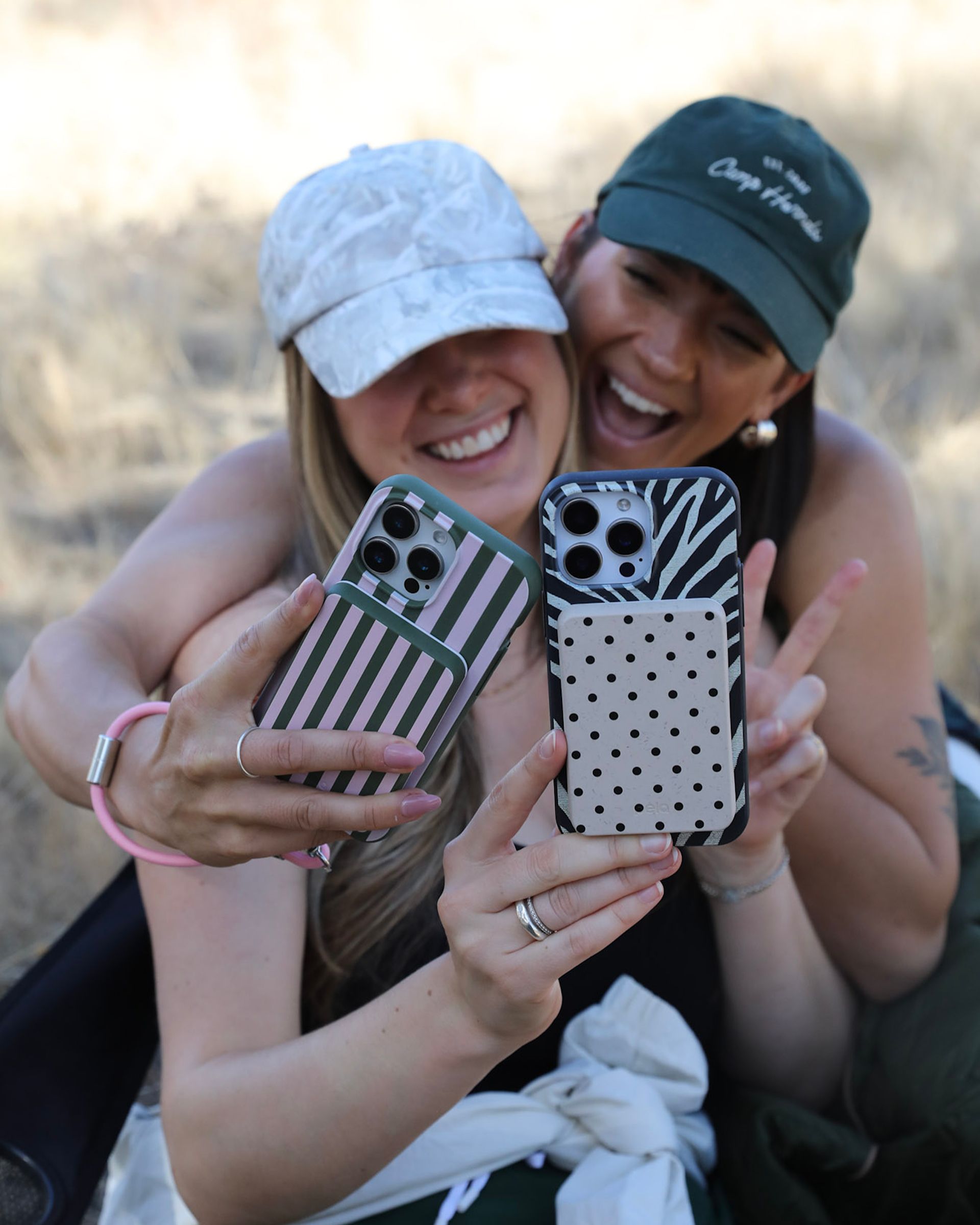 Two smiling women take a selfie, showing off their patterned phone cases outdoors.