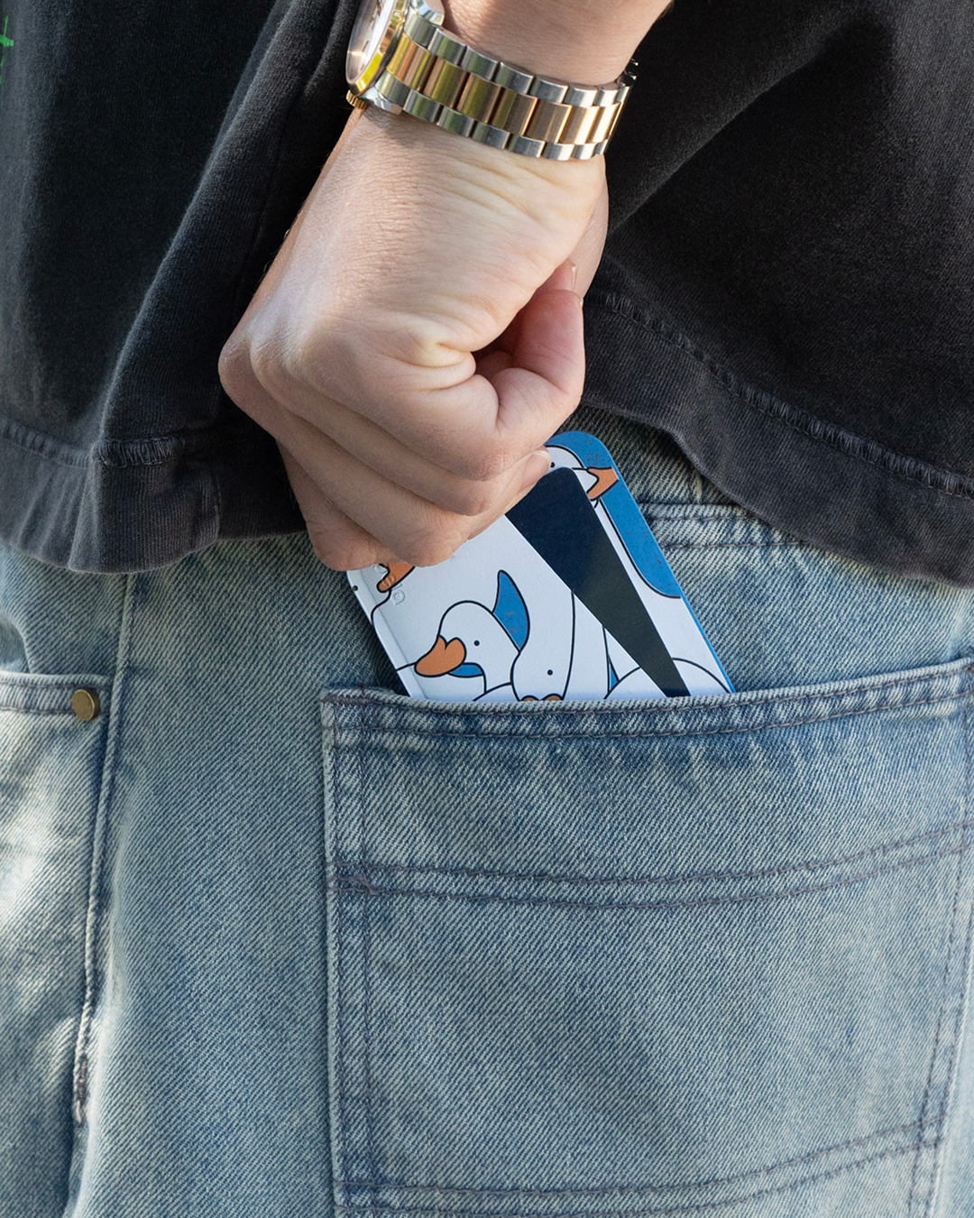 A person places a phone with a cartoon goose case into the back pocket of their blue jeans.