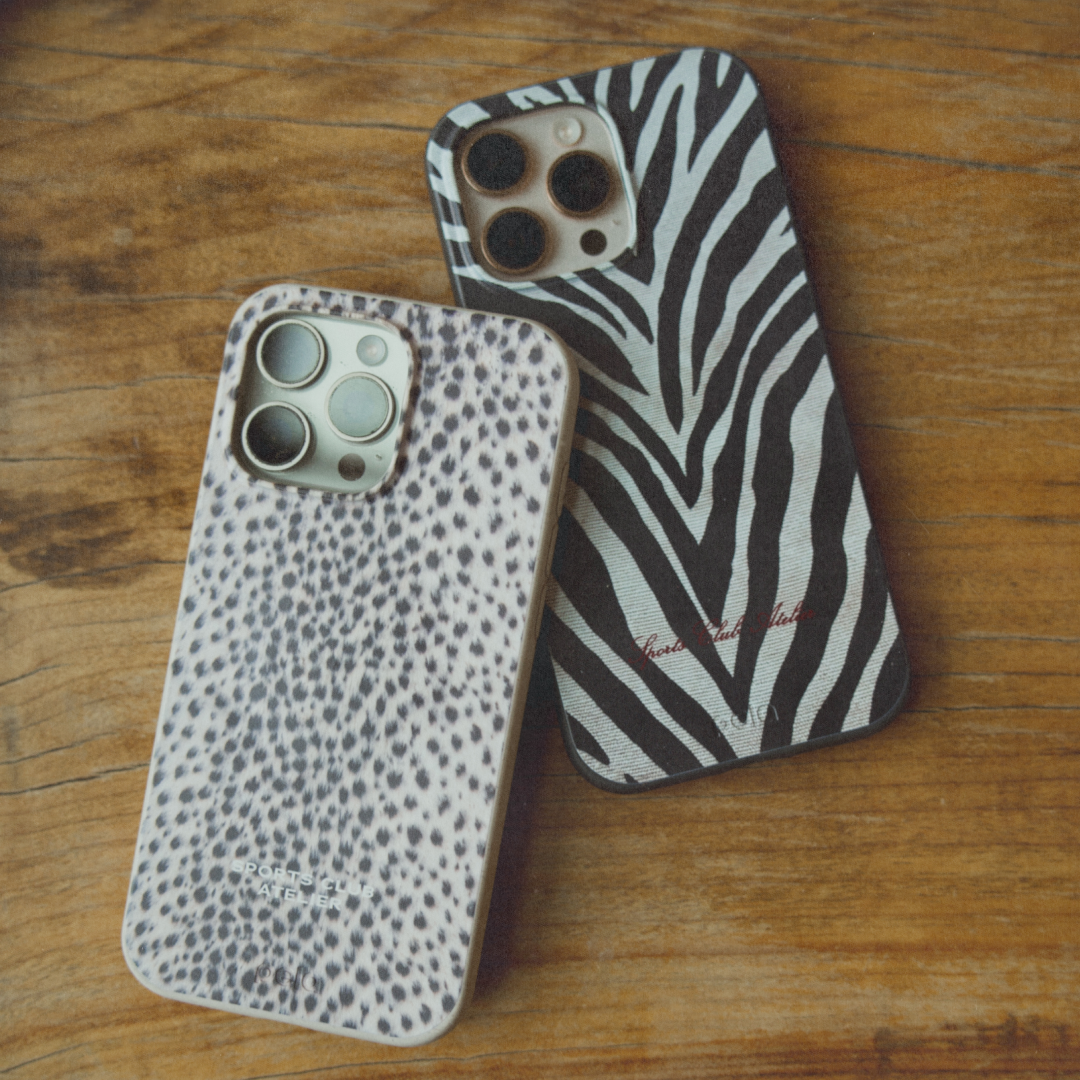 Two iPhones in animal print cases, one spotted and one zebra-striped, on a wooden surface.