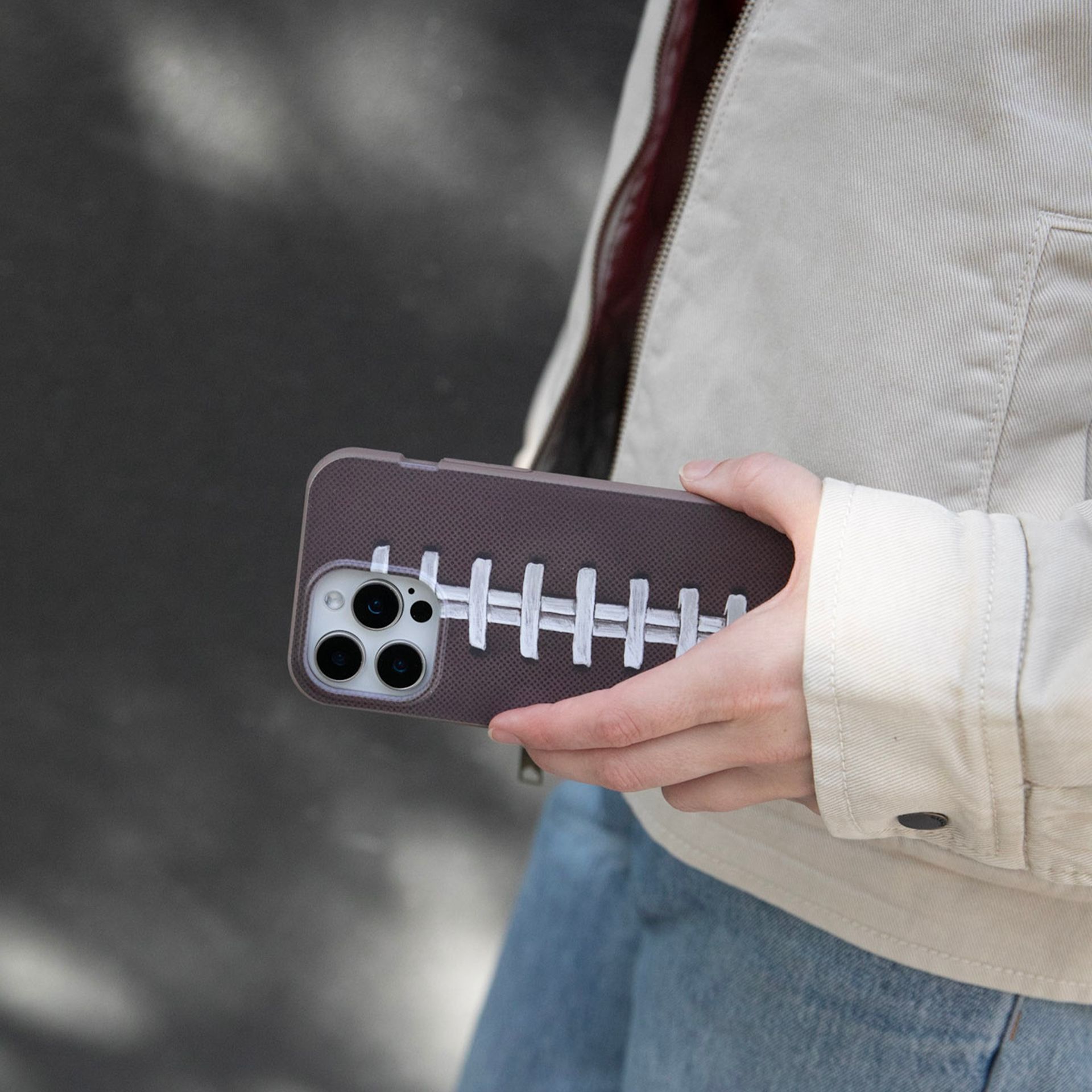 A person holds a phone in a textured brown case that is designed to look like a football.