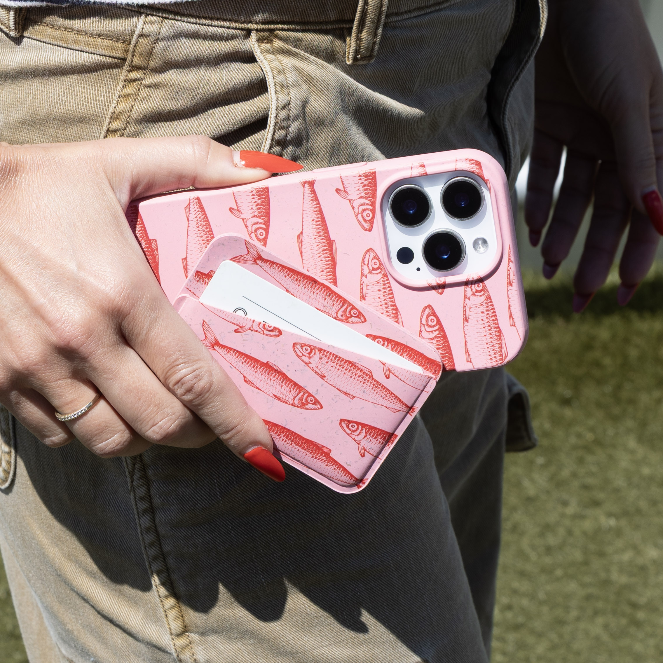 A person holds a pink phone case with a red fish pattern and a matching cardholder.