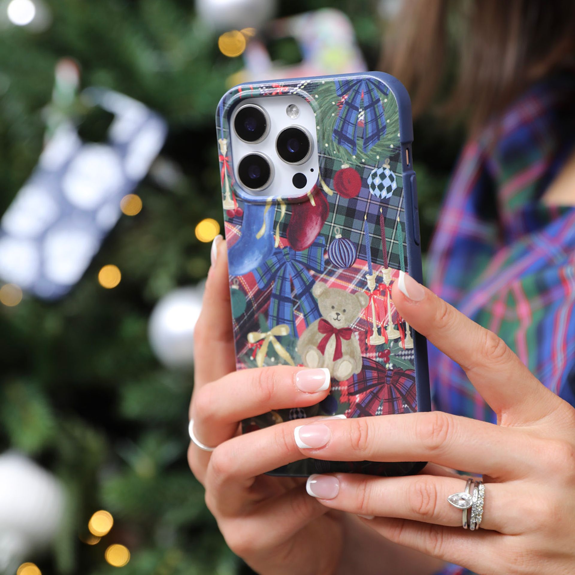 Two women in festive pajamas hold up patterned phone cases in front of a Christmas tree.