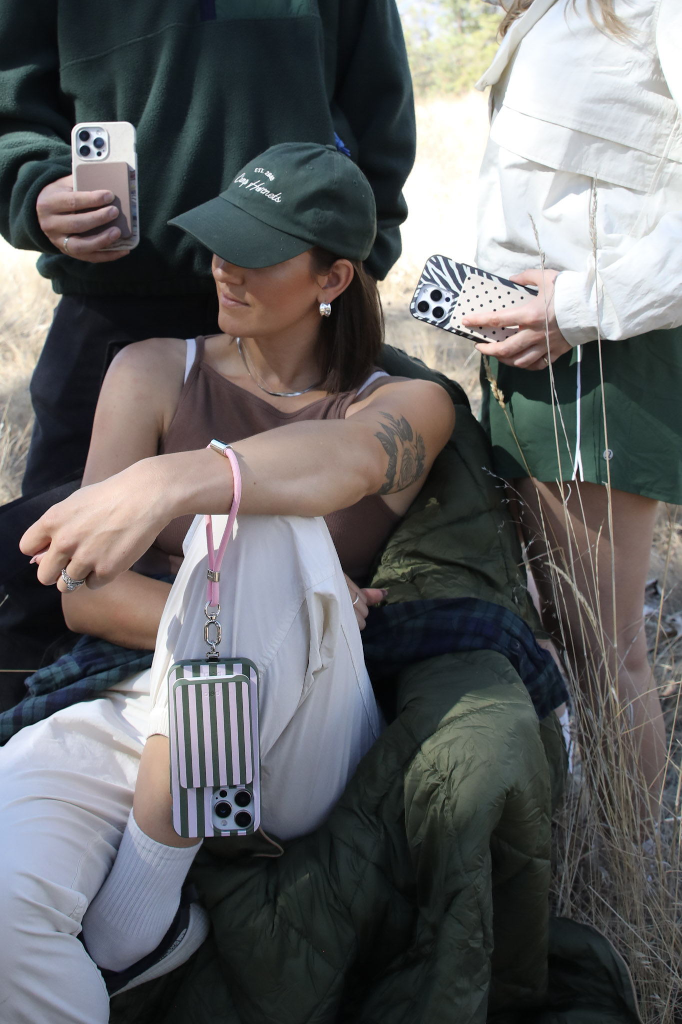 A group of three people outdoors, holding phones with various decorative cases and straps.