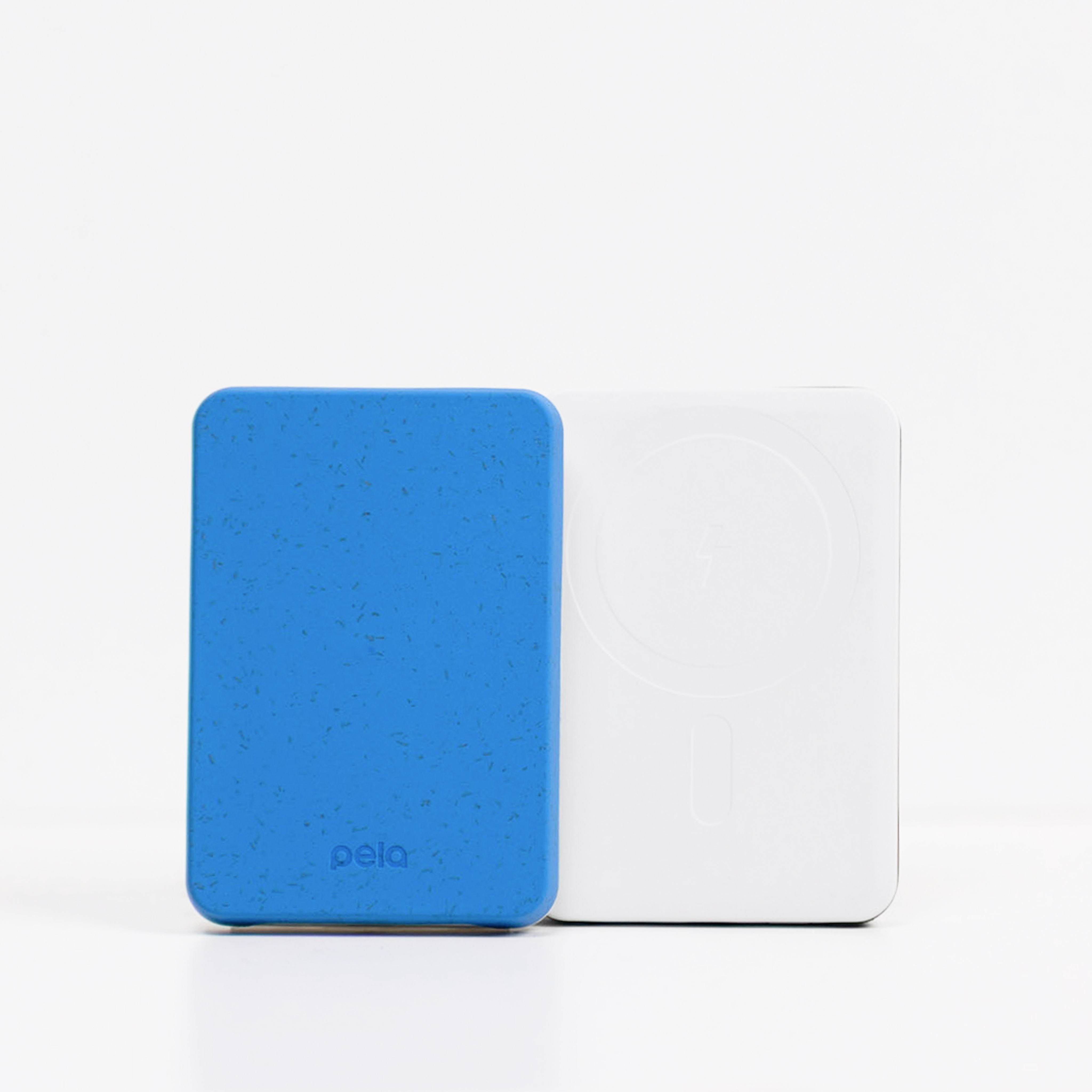 A blue speckled Pela case stands next to a white wireless charging pad on a white surface.