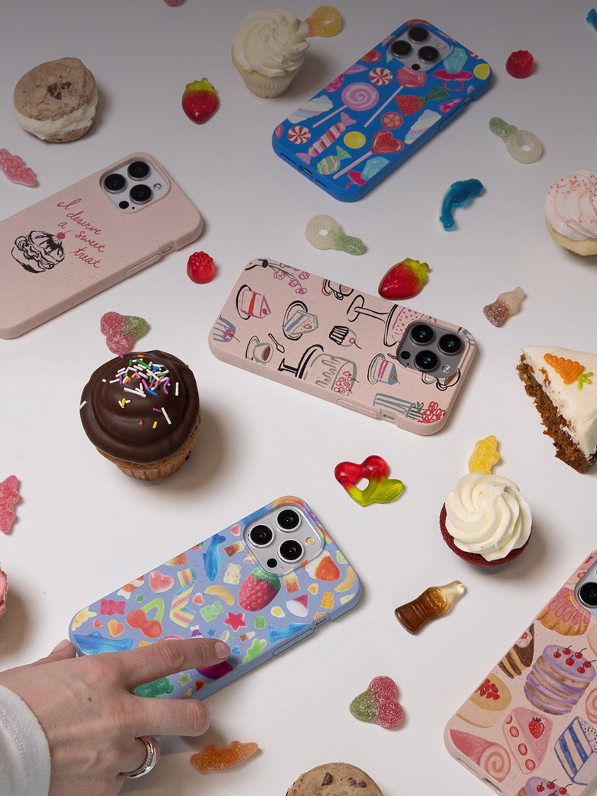 A flat lay of several candy and dessert-themed phone cases surrounded by cupcakes and gummy candies.