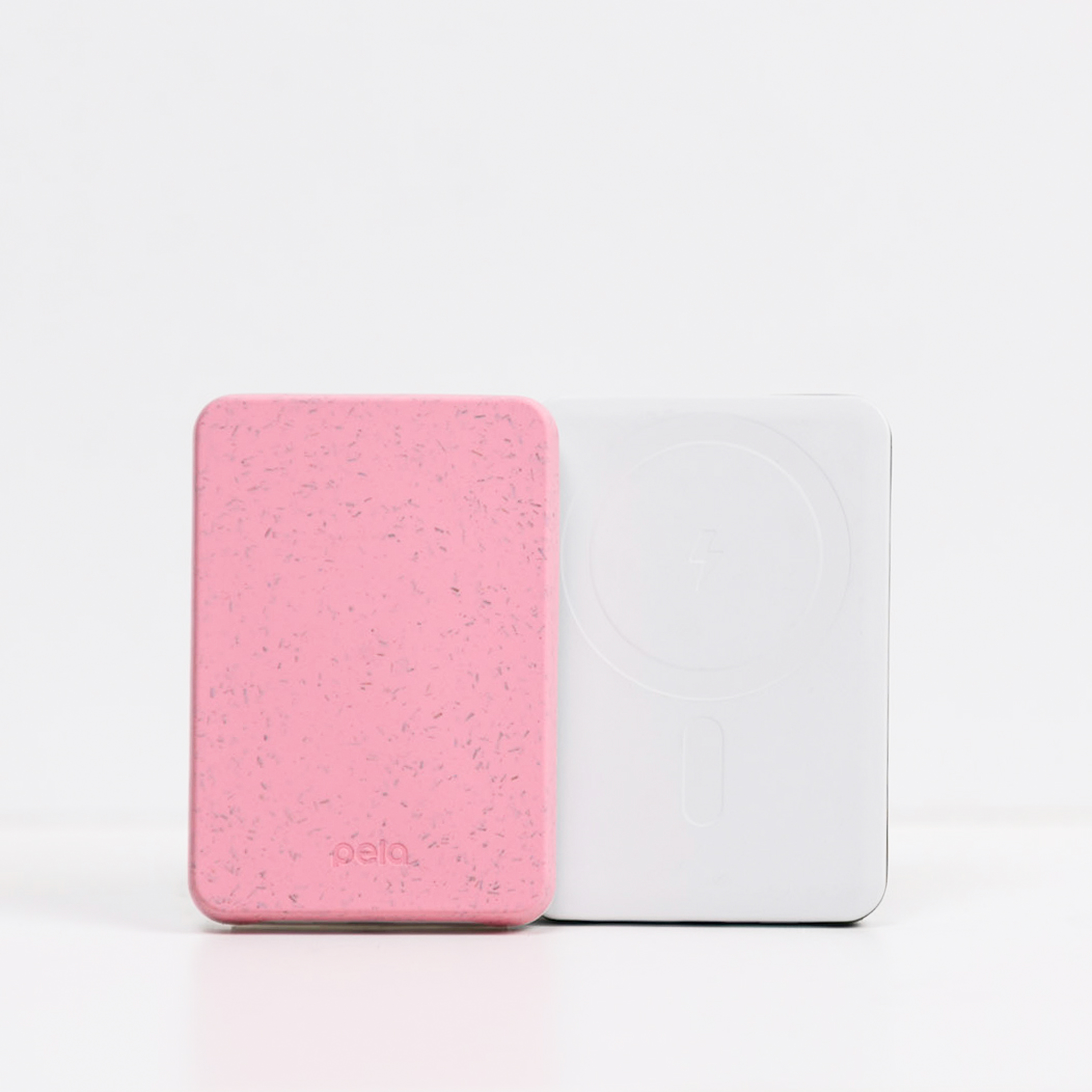 A pink speckled Pela power bank leans against a white wireless power bank on a white surface.