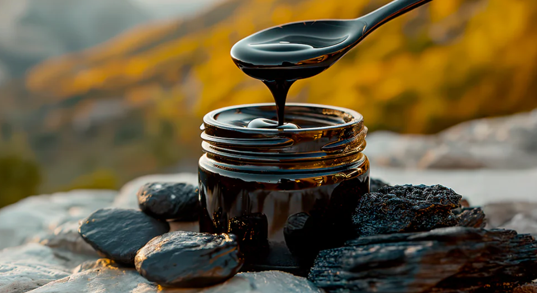 A jar of black liquid with a spoon, surrounded by rocks.