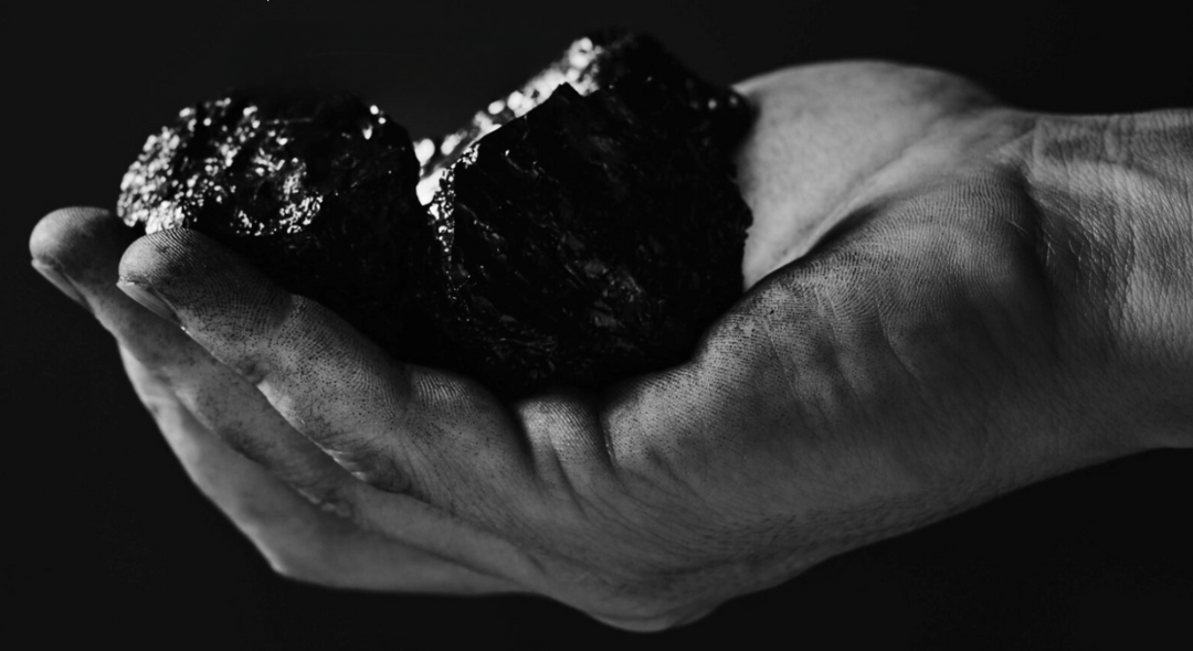 Dirty hand holding a piece of coal in black and white.