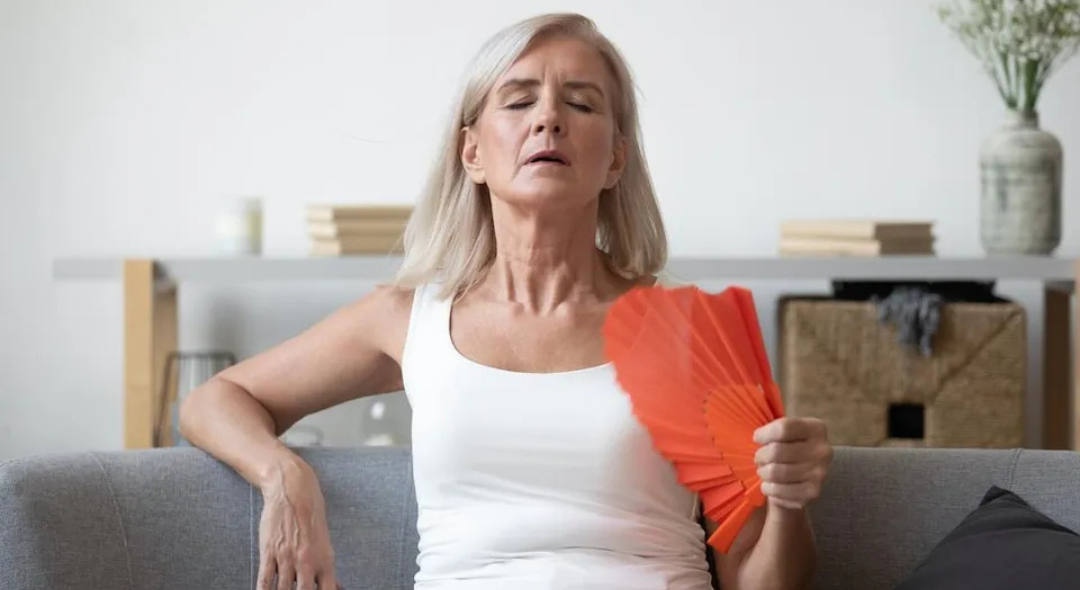 Older woman fanning herself while sitting on a couch.