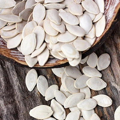 A bowl spilling white pumpkin seeds onto a wooden surface.