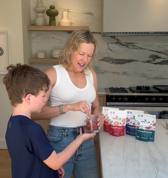 Woman and child in kitchen mixing drink with packets on counter.