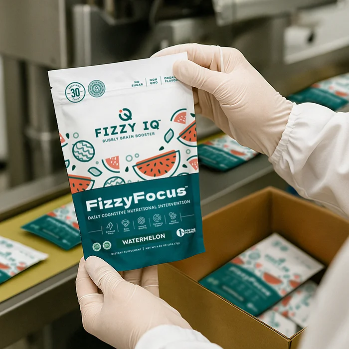 Person holding a packet of FizzyFocus dietary supplement in a factory setting.