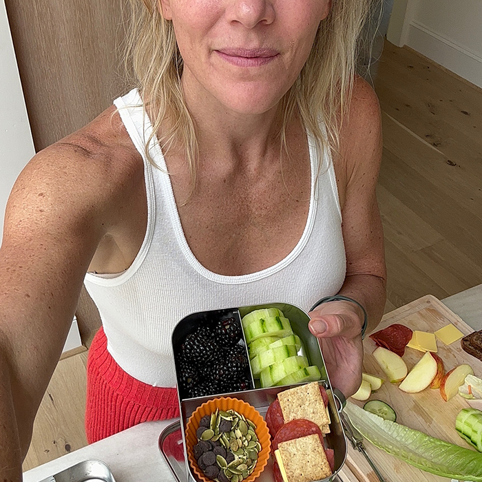 Person holding a lunchbox with fruits, vegetables, and snacks.