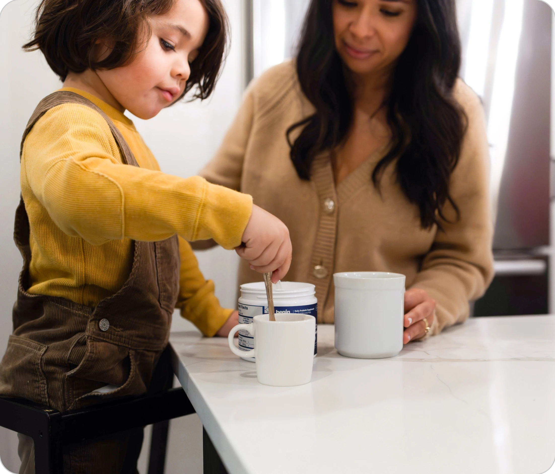 Child stirring a cup with an adult watching in a kitchen setting.