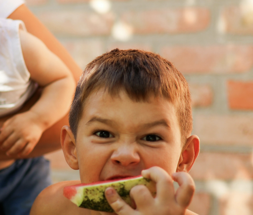 Child drinking juice with a straw; hand pouring packet into a colorful pitcher.