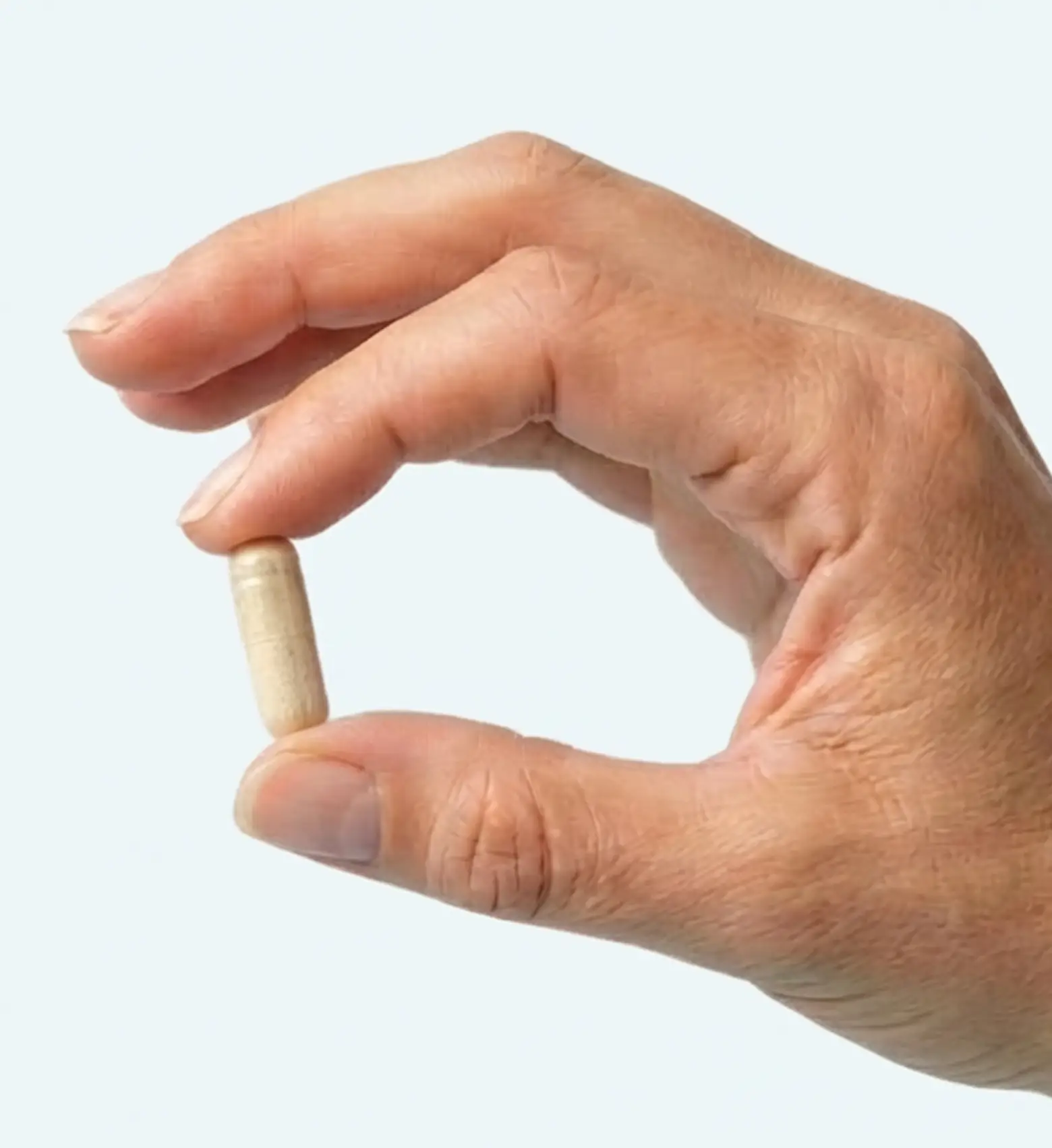 A close-up of a hand holding a single, light-colored capsule between the thumb and forefinger.