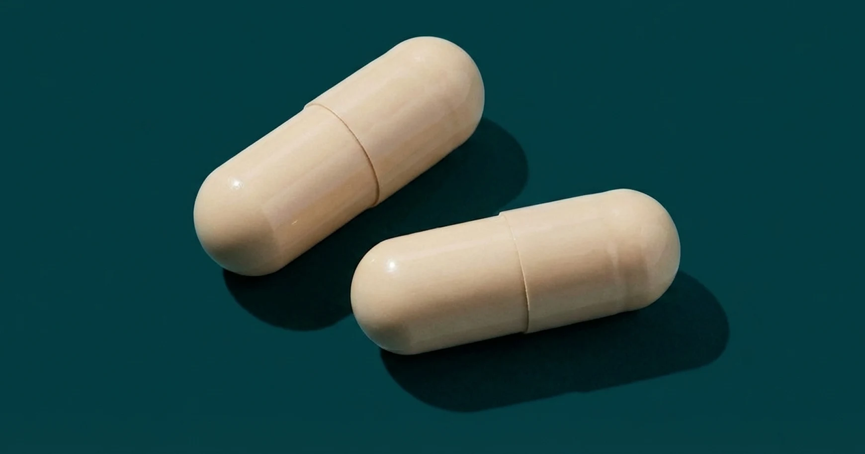 A close-up photograph of two off-white capsules on a dark teal background.