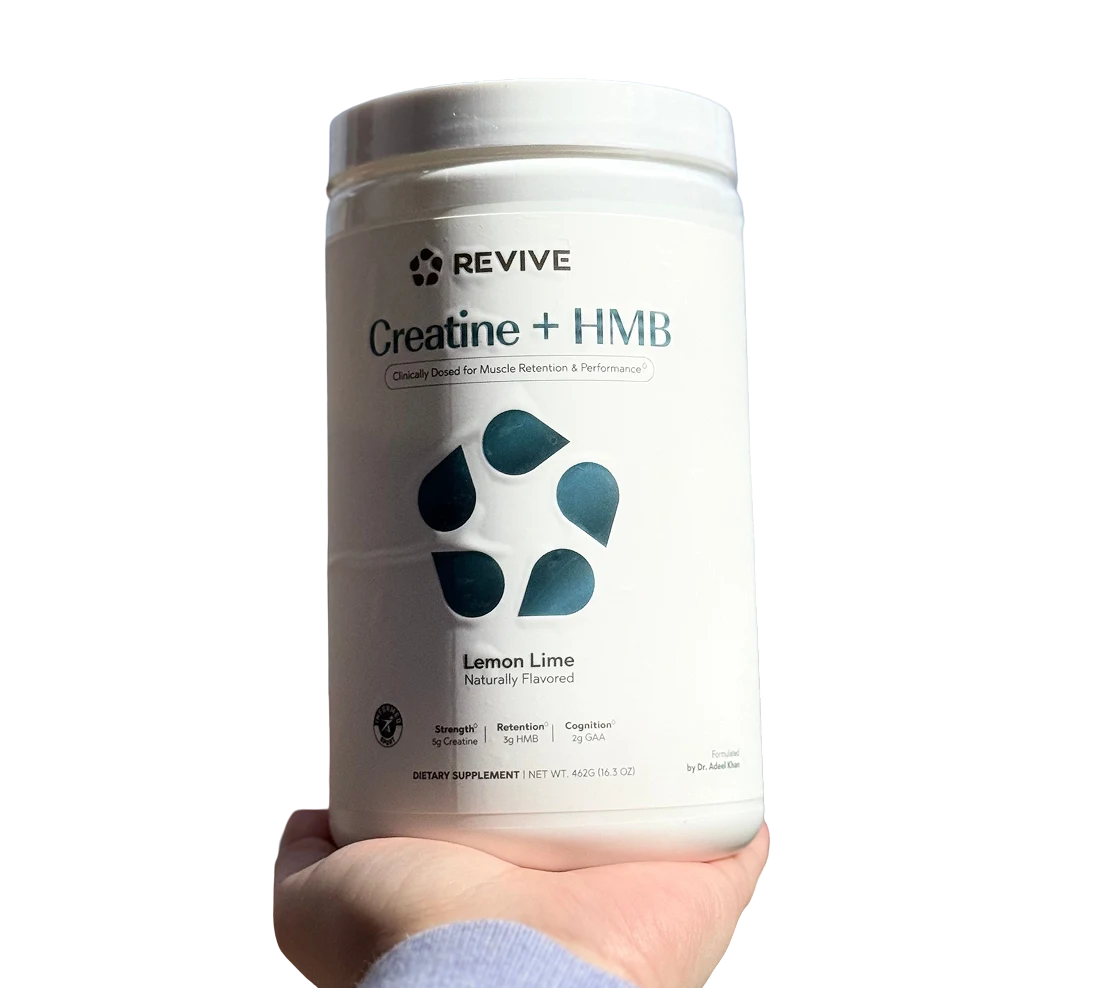 A hand holds a white tub of Revive Creatine + HMB dietary supplement in Lemon Lime flavor.