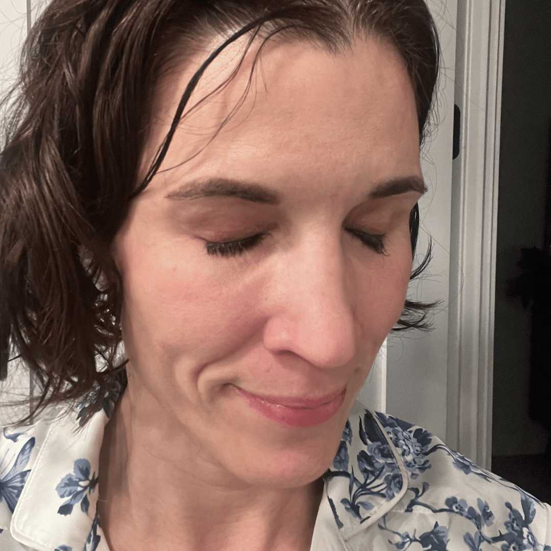 A woman with short, wet brown hair smiles with her eyes closed while wearing a floral pajama top.