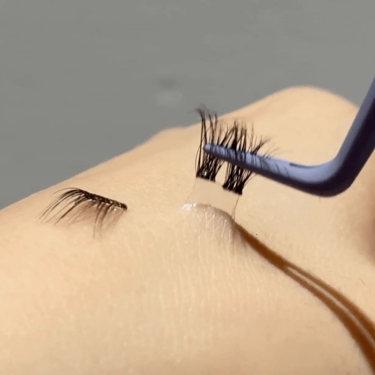 Tweezers applying false eyelashes on a surface.
