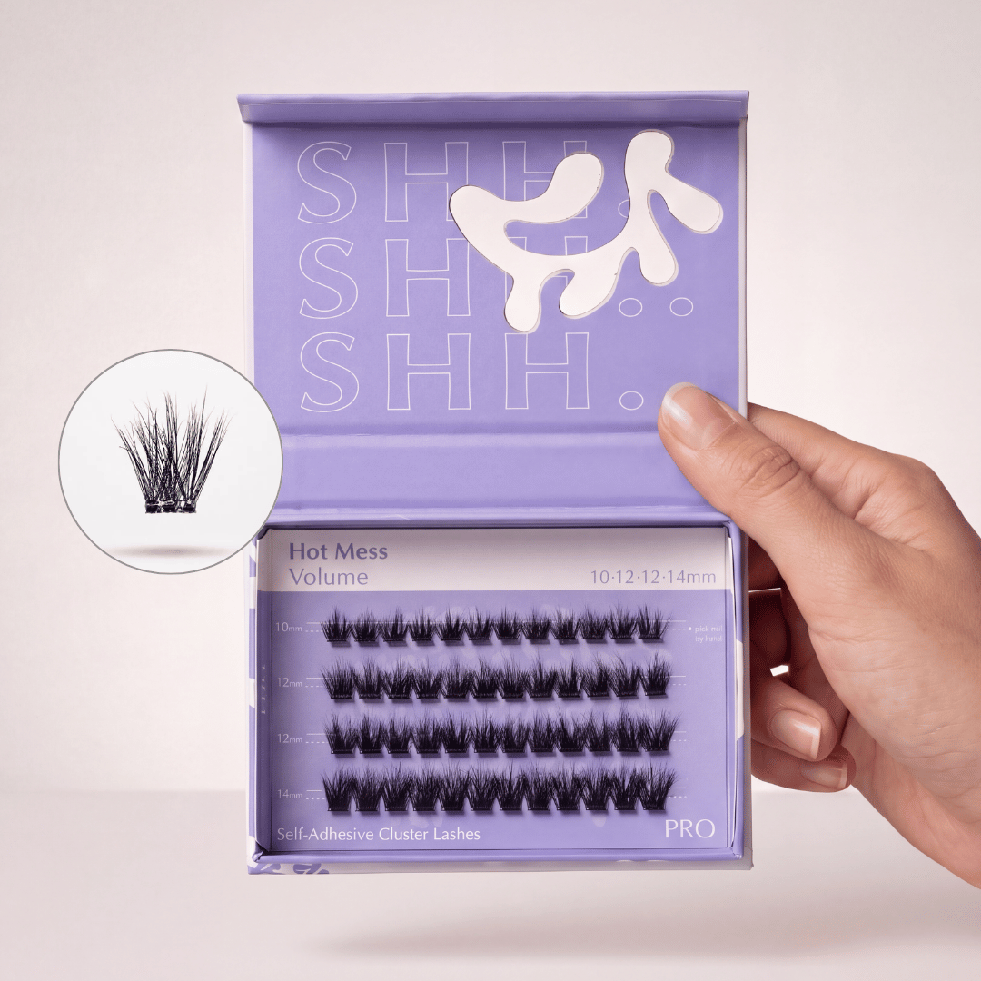 A hand holding an open purple box of 'Hot Mess Volume' self-adhesive cluster lashes.