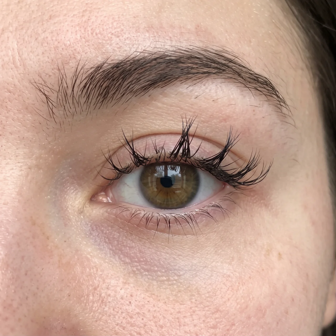 A close-up of a person's brown eye, showing long, spiky false eyelashes and a dark eyebrow.
