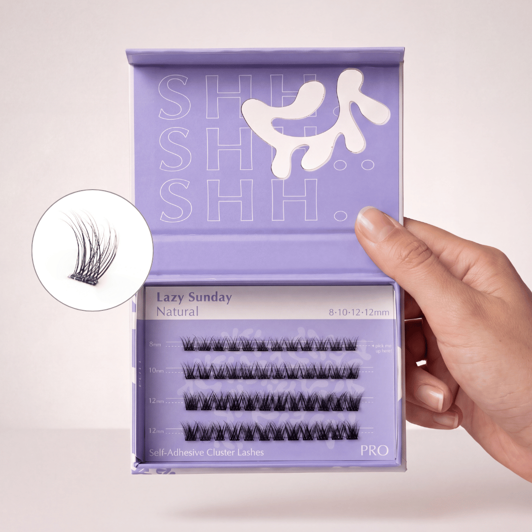A hand holds open a purple box of 'Lazy Sunday Natural' self-adhesive cluster eyelashes.