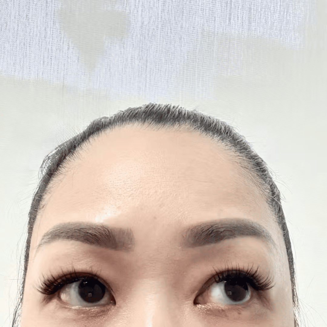 A close-up of a woman's forehead and eyes with long eyelash extensions, looking up and to the right.