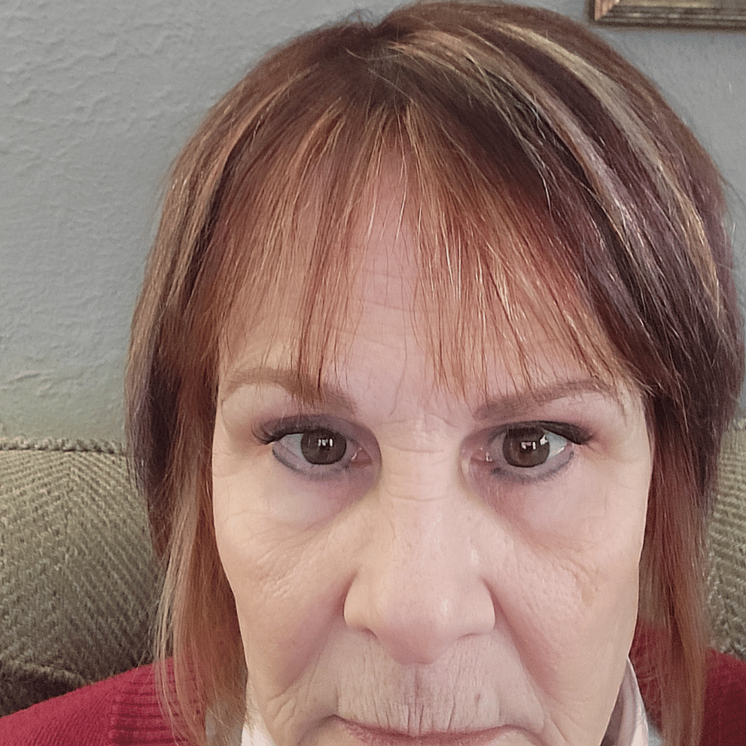 A close-up photo of a woman with reddish-brown hair with bangs, looking directly at the camera.