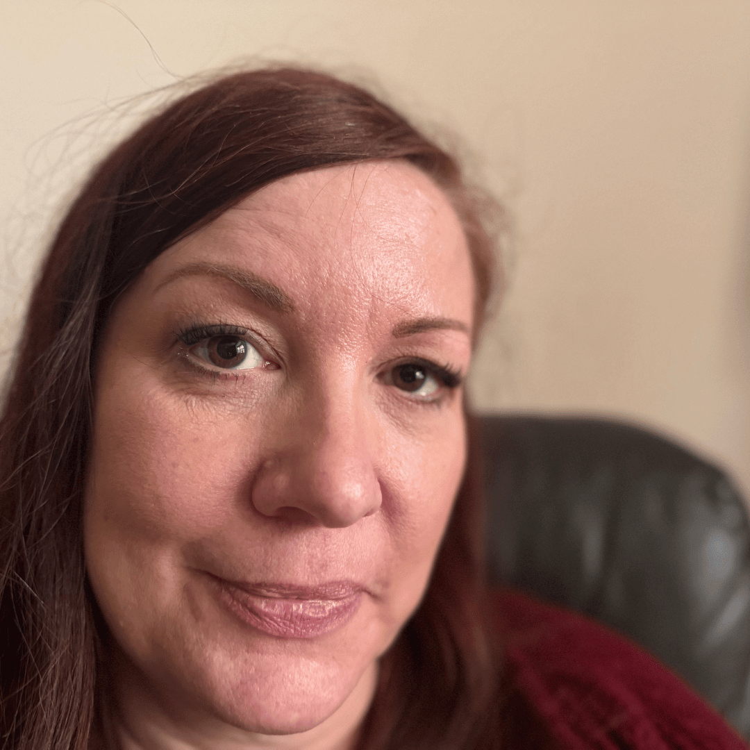 A close-up headshot of a woman with reddish-brown hair and brown eyes looking directly at the camera.