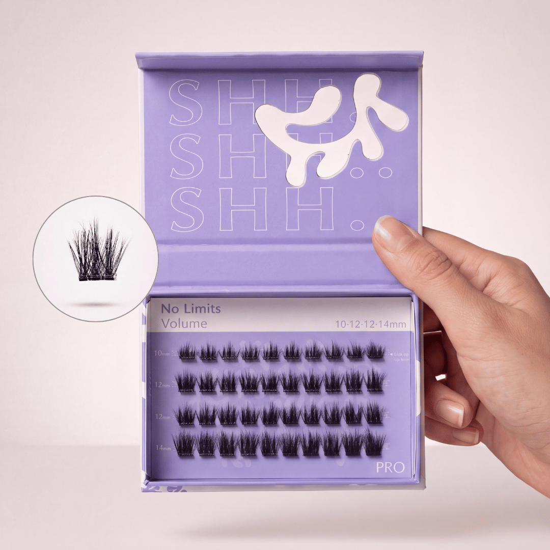 A hand holds an open purple box of 'No Limits Volume' eyelash extensions in various lengths.