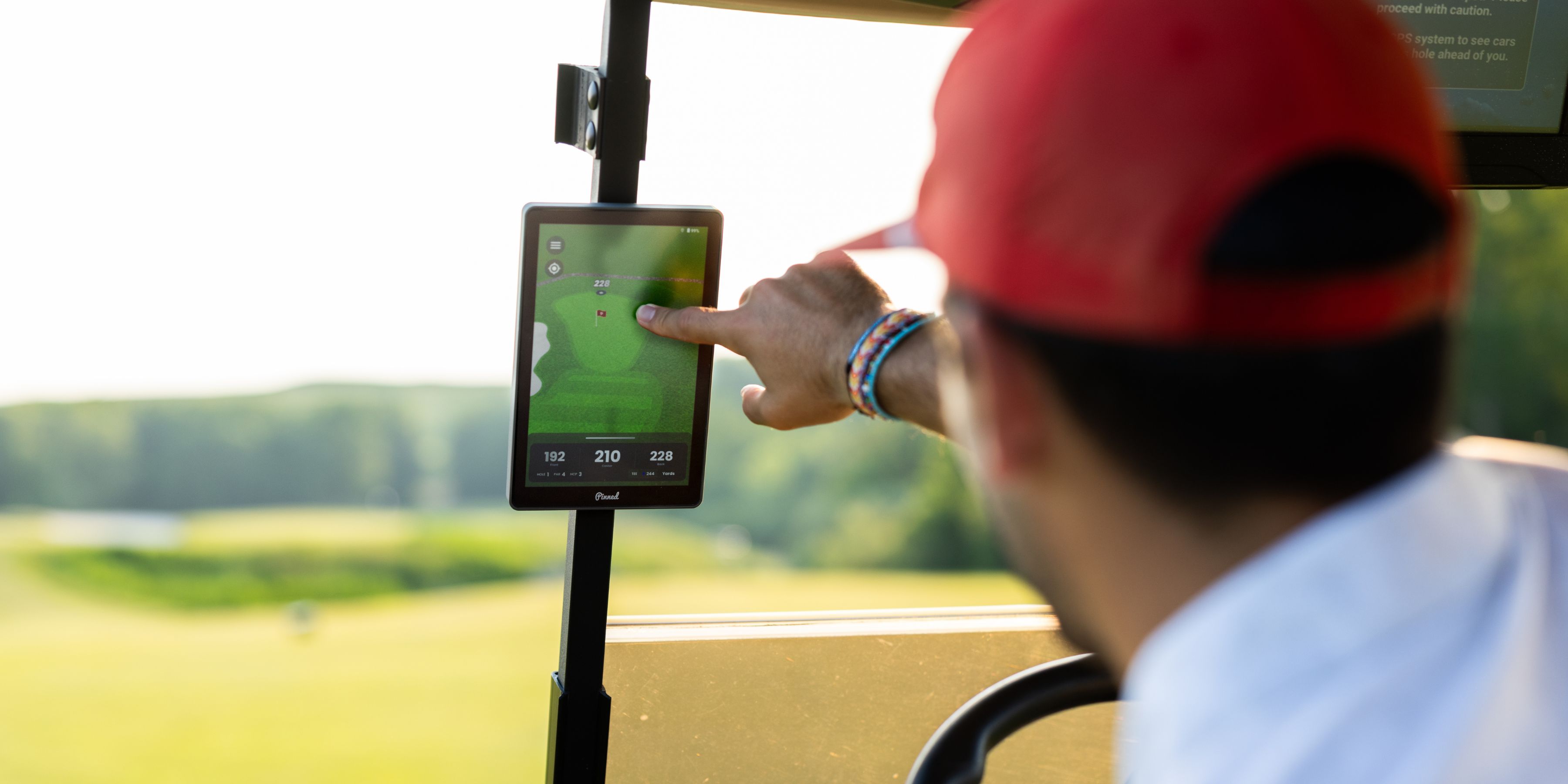 A person in a red hat in a golf cart points to a GPS screen showing the course layout.