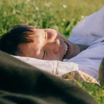 Person smiling while lying on grass in sunlight.