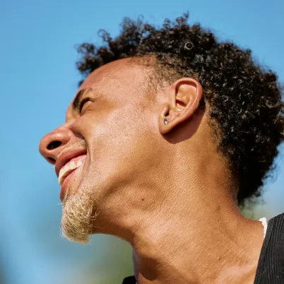 Man smiling, head tilted back, against blue sky background.