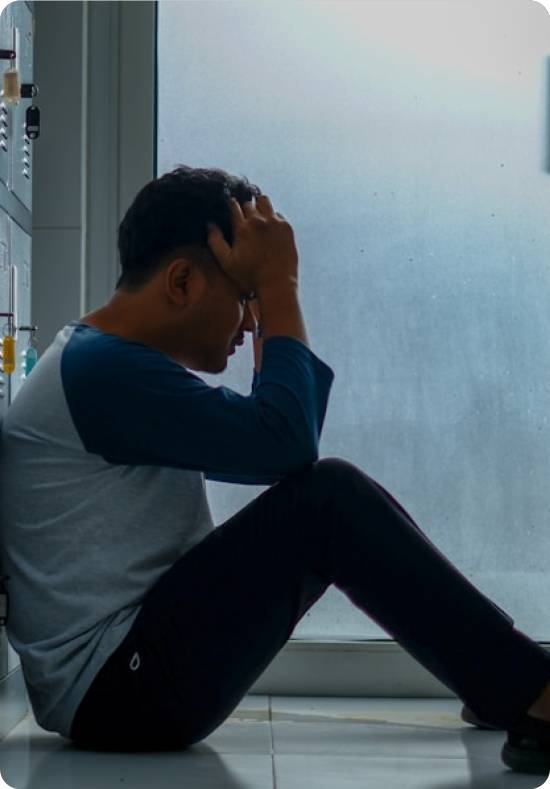 Person sitting on the floor, holding head in hands, looking distressed.