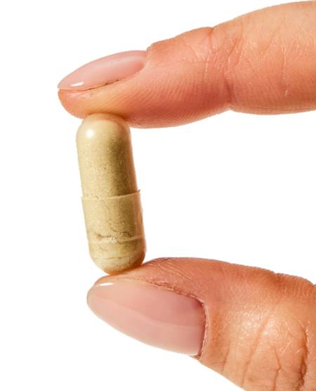 A hand holding a beige capsule between fingers.