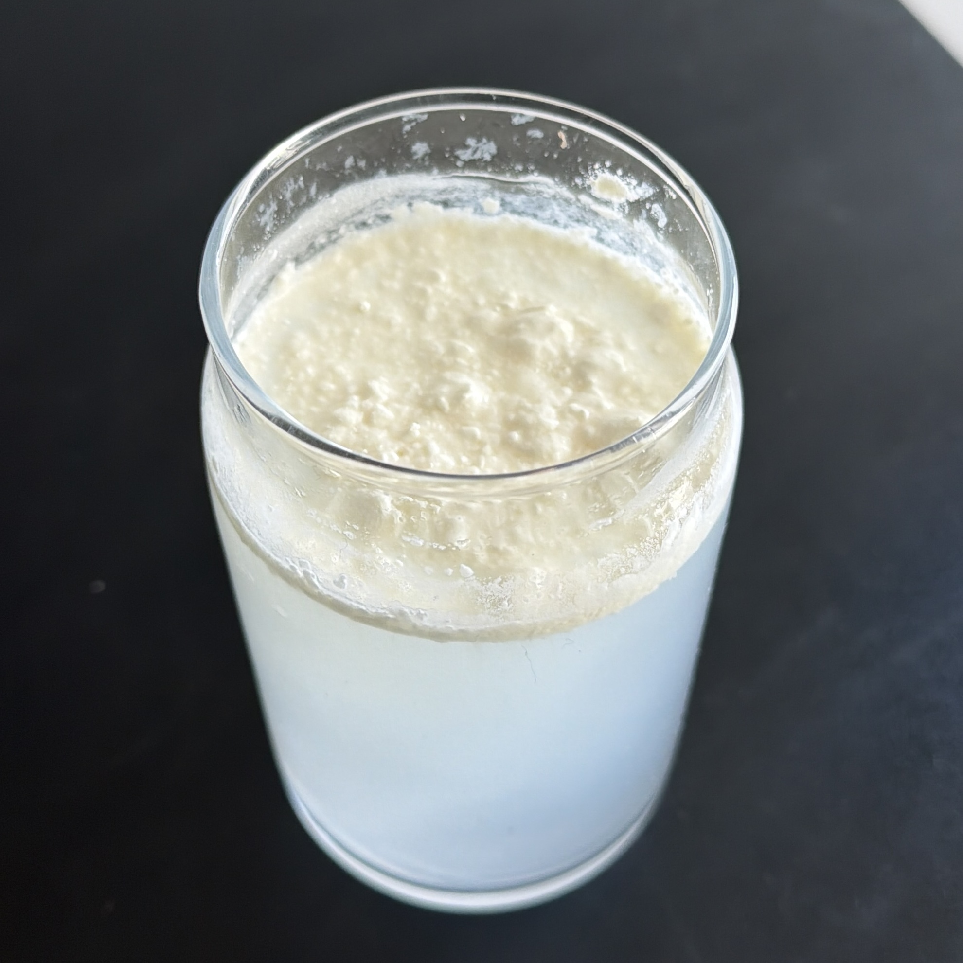 A glass jar of separated liquid, with a thick layer of curds floating above the whey.