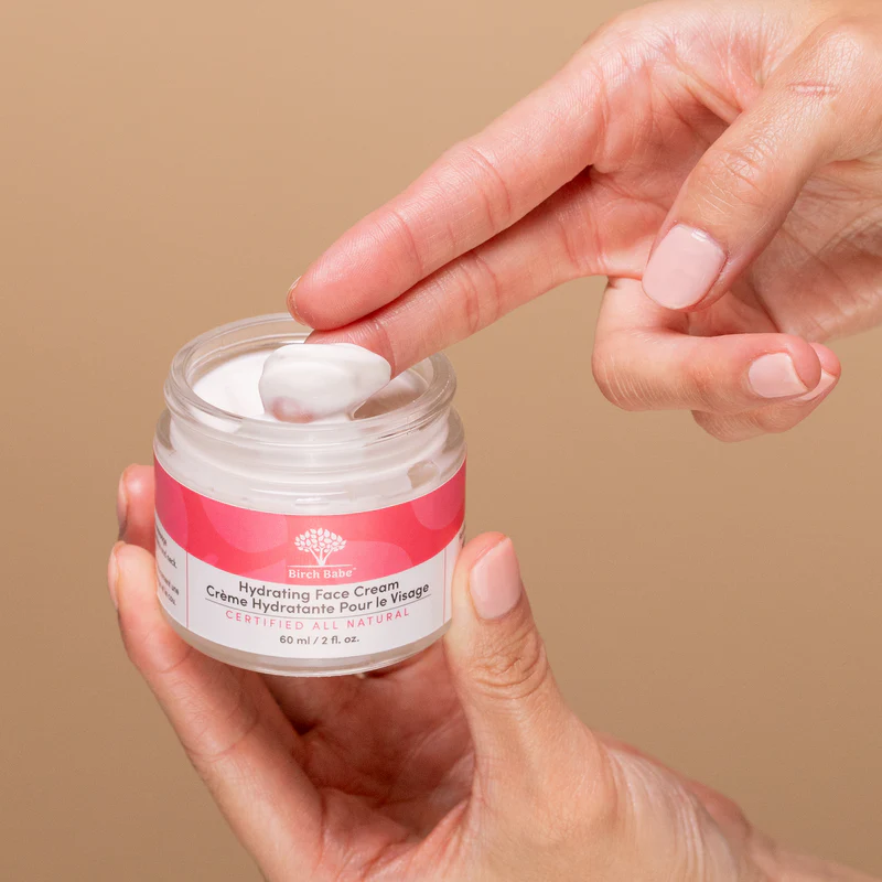 Hand holding and using a jar of hydrating face cream.