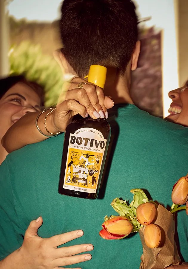 Person holding a Botivo bottle and bouquet of tulips, surrounded by smiling friends.