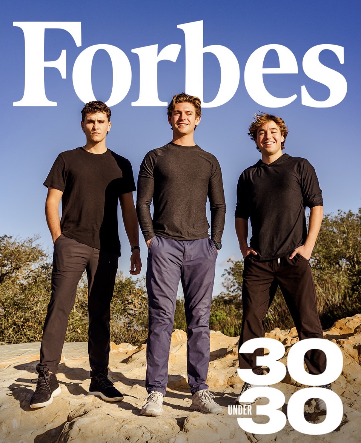 Three people standing outside on rocky ground beneath the 'Forbes 30 Under 30' text.
