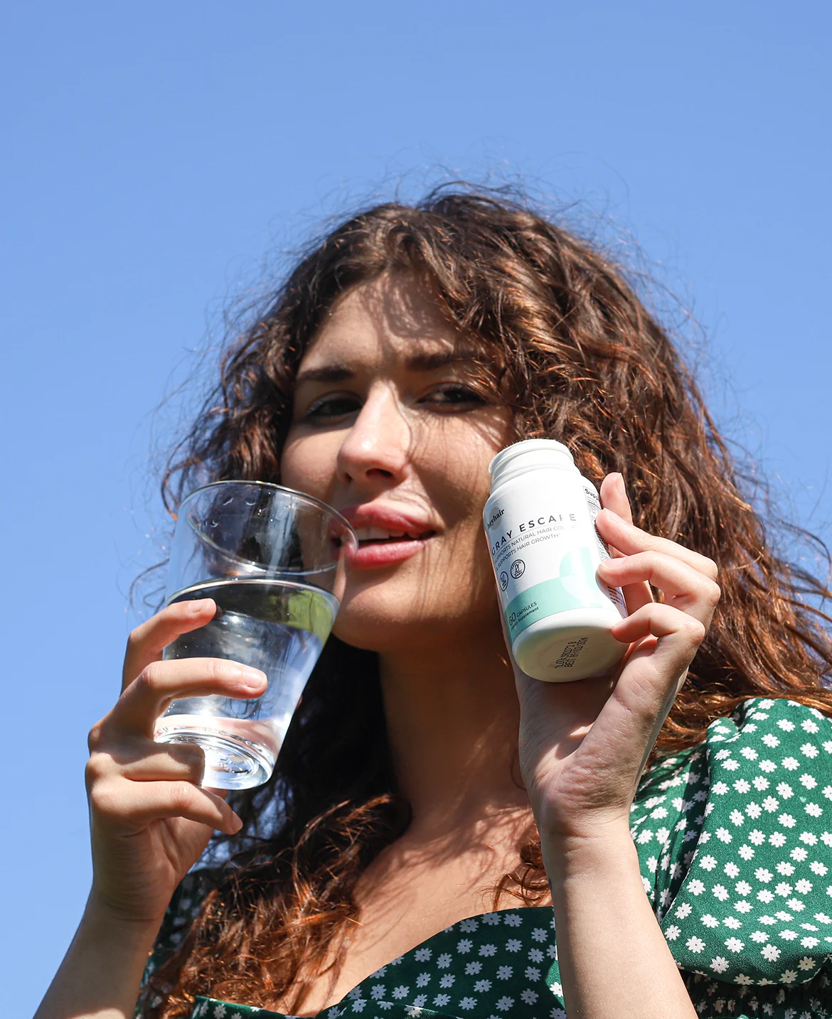 Woman holding a glass of water and a bottle against a clear blue sky.