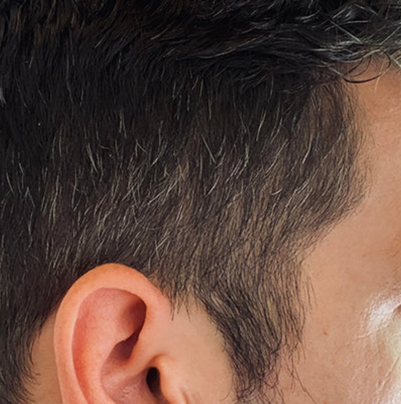 Close-up of a person's ear and side of the head with short dark hair.