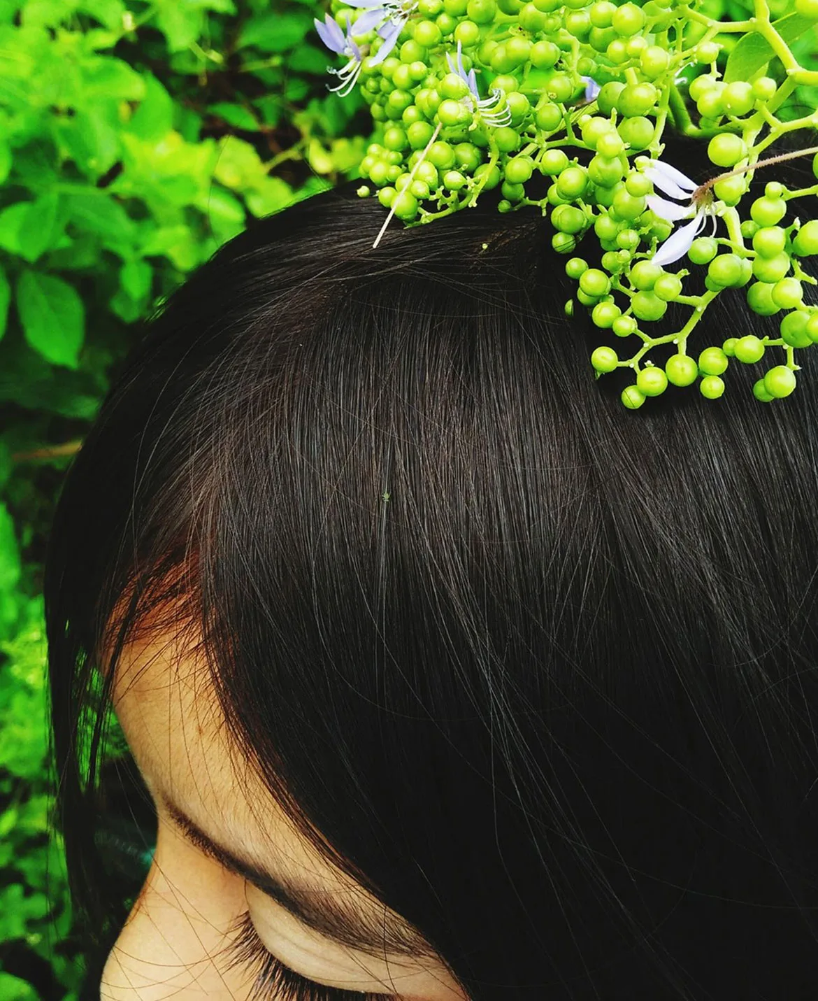 Close-up of a person with green berries and leaves on their head.