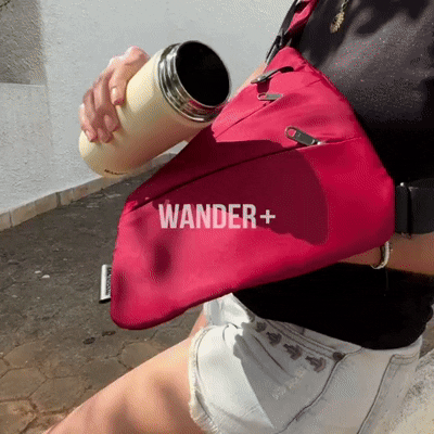 Person wearing a red WANDER+ crossbody bag, pouring from a yellow thermos.