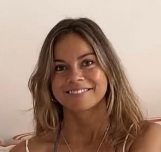 A close-up of a smiling woman with long, light brown hair looking towards the camera.