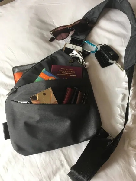 Black bag with contents including passport, sunglasses, keys, and lipsticks on a white surface.