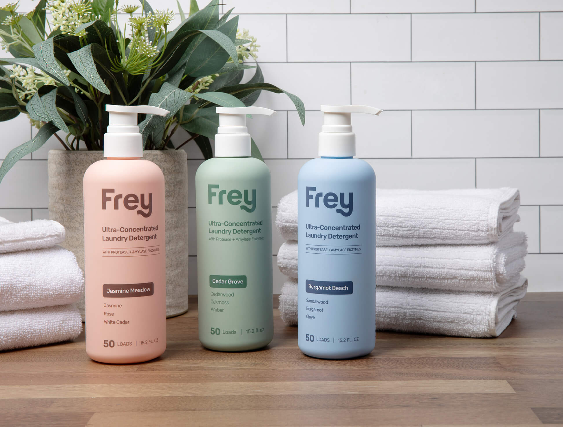 Three Frey laundry detergent bottles with towels and a plant in the background.